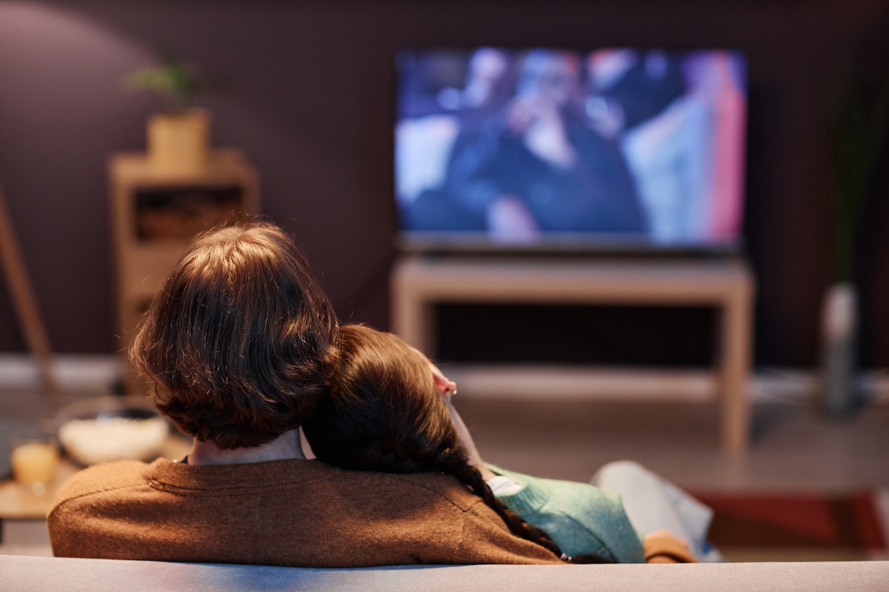 Back view of young couple watching TV together at home sitting on sofa in dark